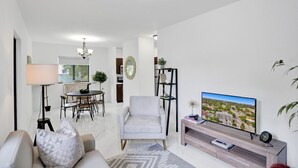 A modern living room with a sofa, armchair, dining table, and TV. -  Renzzi Wynwood Apartments (Miami)