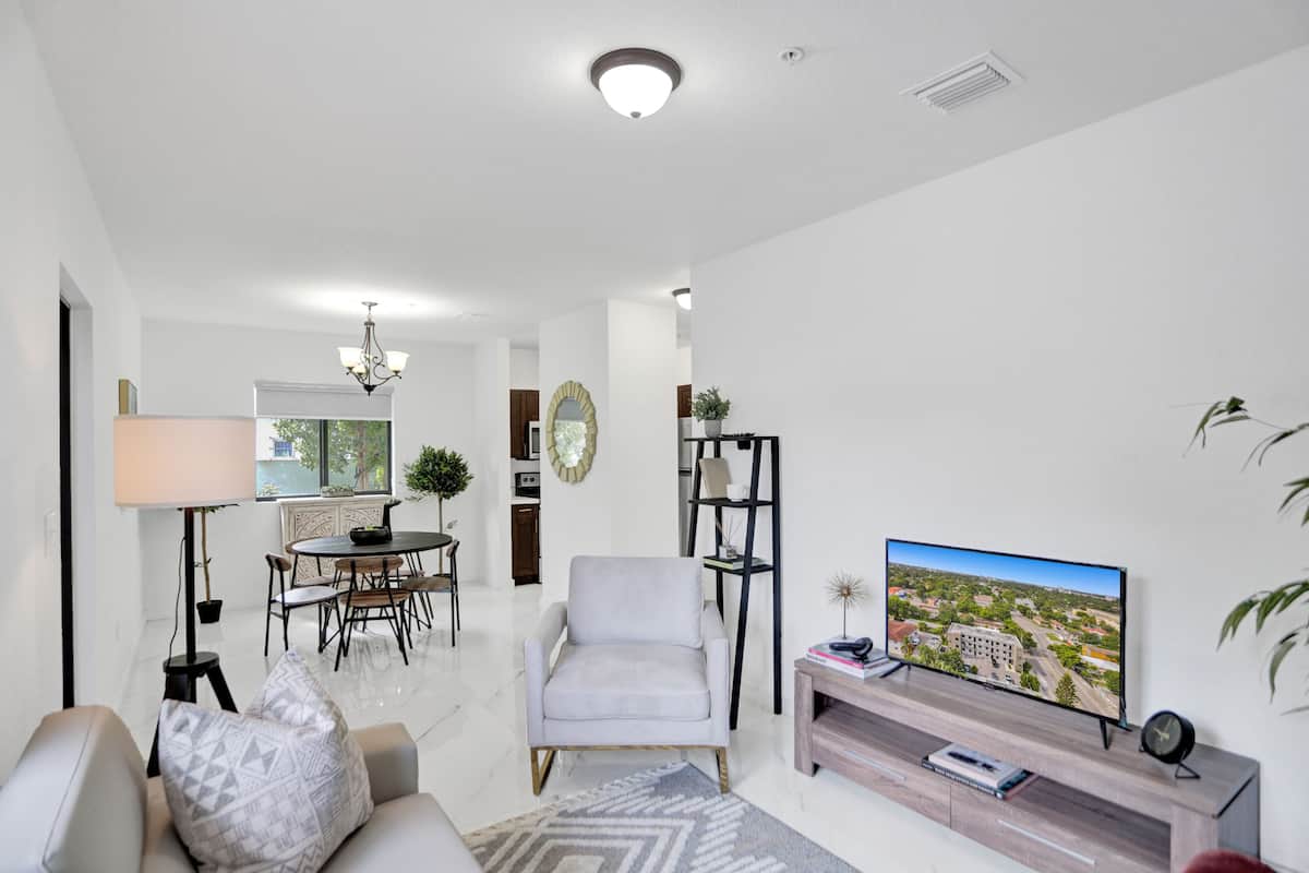 A modern living room with a sofa, armchair, dining table, and TV.