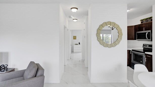 A modern interior with a hallway leading to a kitchen area, featuring white walls, a grey sofa, and a decorative mirror. -  Renzzi Wynwood Apartments (Miami)