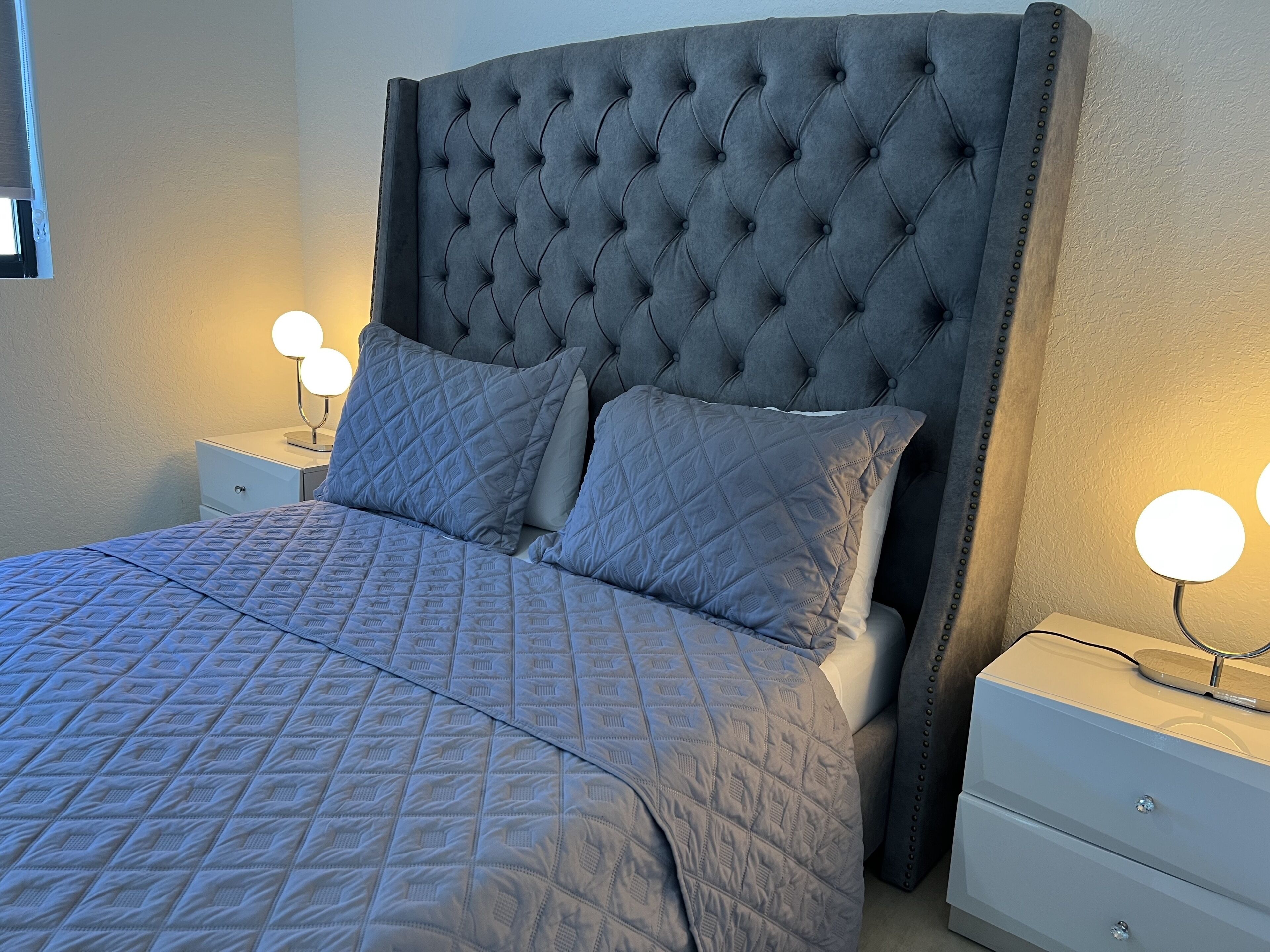 A neatly made bed with a tufted headboard, two bedside lamps, and a quilted bedspread.