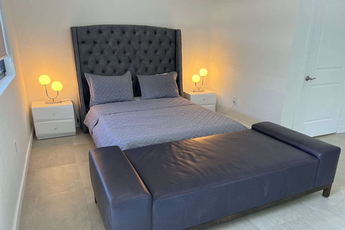A bedroom with a bed, two bedside tables, a bench, and two wall-mounted lamps.