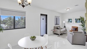 A modern living room with a white dining table, grey sofa, and a chandelier. -  Renzzi Wynwood Apartments (Miami)