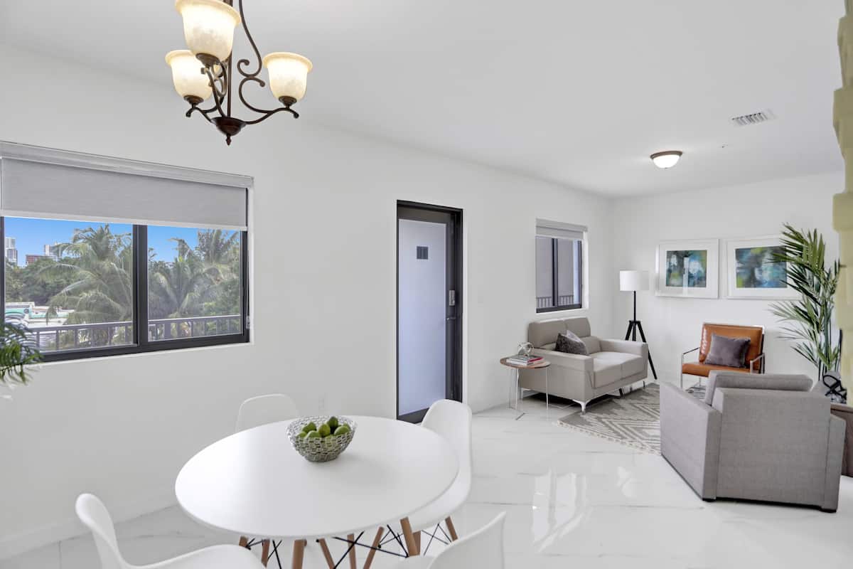 A modern living room with a white dining table, grey sofa, and a chandelier.