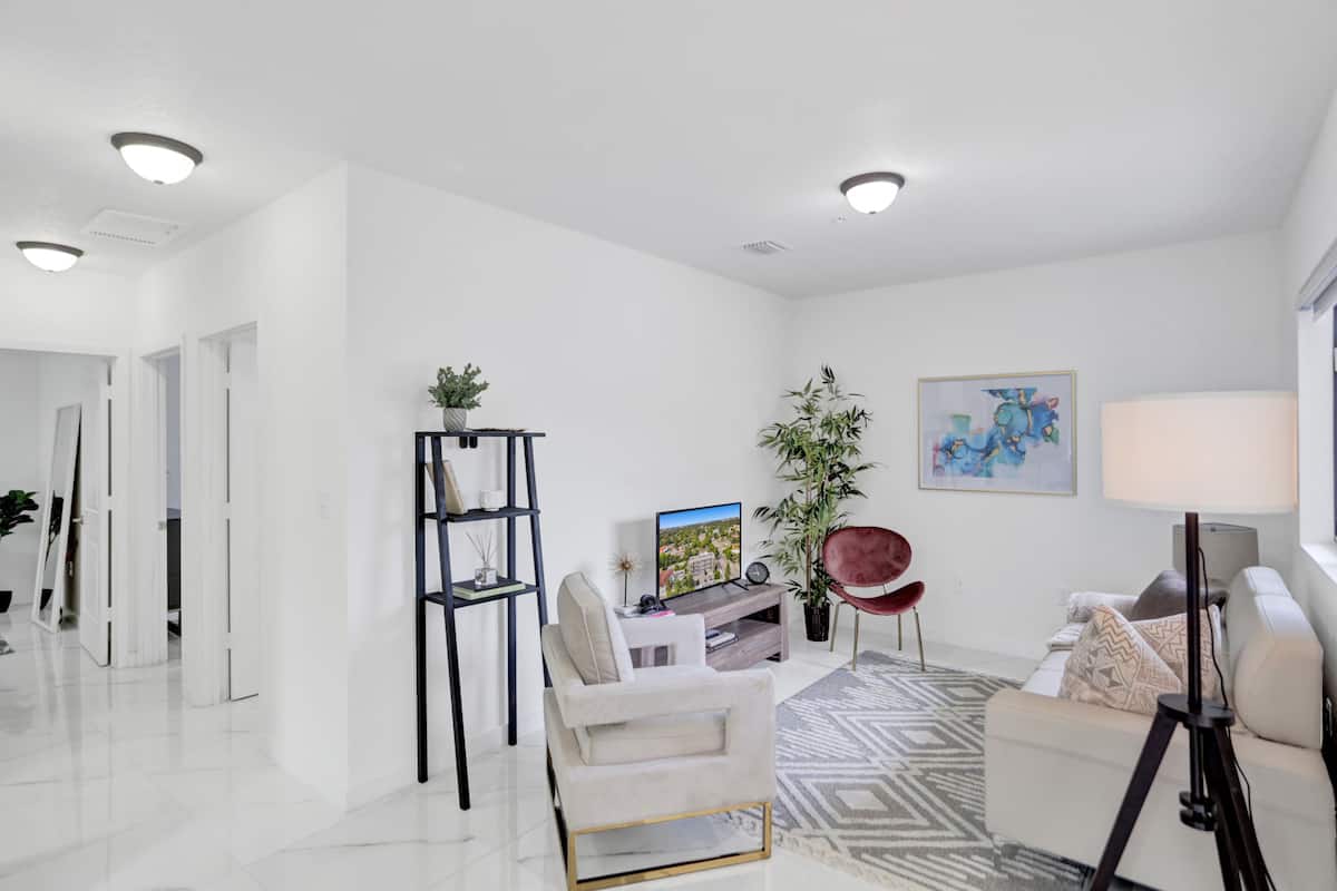 A modern living room with a white sofa, a red chair, a TV on a wooden stand, a potted plant, and a painting on the wall.