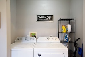 Un lavadero con dos lavadoras Whirlpool y un estante con productos de limpieza.