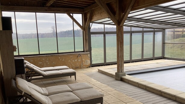 Ein überdachter Poolbereich mit Liegestühlen und Blick auf ein großes Gewässer.