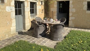 Ein rustikaler Außenbereich mit Korbstühlen und einem Tisch, umgeben von einem Garten mit gelben Blumen.