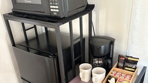 Pieni, käytännöllinen keittiö, jossa on musta mikroaaltouuni, kahvinkeitin ja säilytystilaa tarjoavat laatikot.