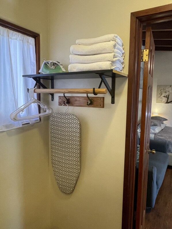 A room with a wooden shelf holding folded towels and a hanging garment steamer.