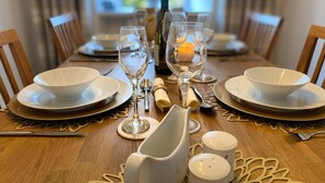 Una mesa de comedor dispuesta con cuencos, platos y cubiertos blancos, junto con una botella y velas en el centro.