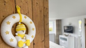 Un adorno de muñeco de nieve tejido cuelga de una pared de madera en una habitación de hotel, con una cama y un televisor al fondo.