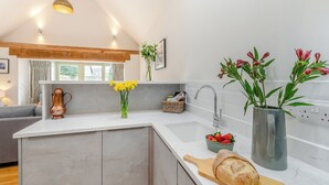 Eine moderne Küche mit Marmorarbeitsplatte, einer integrierten Kochinsel, einer Pendelleuchte und Blick ins Wohnzimmer.