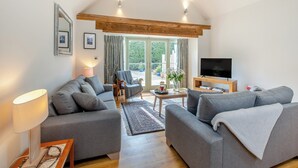 Ein modernes Wohnzimmer mit grauen Sofas, einem Fernseher und einem Holzbalken an der Decke.
