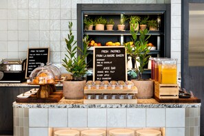 A bakery counter with fresh pastries, a juice bar, and a display of fruits. - Hyatt Place Melbourne, Caribbean Park (Scoresby)