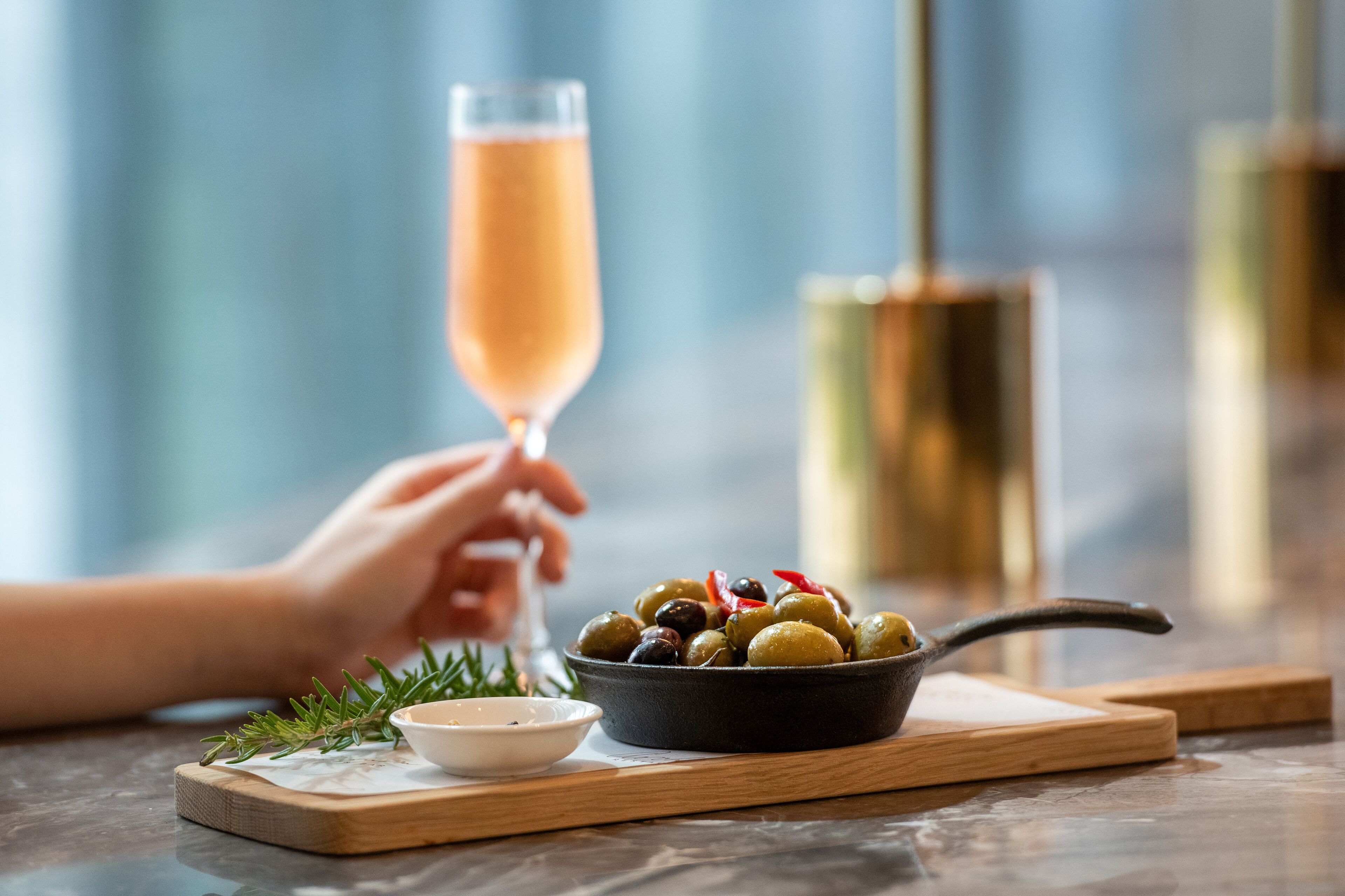 Una mesa con un bol de aceitunas, un recipiente pequeño de condimentos y una copa de champán.