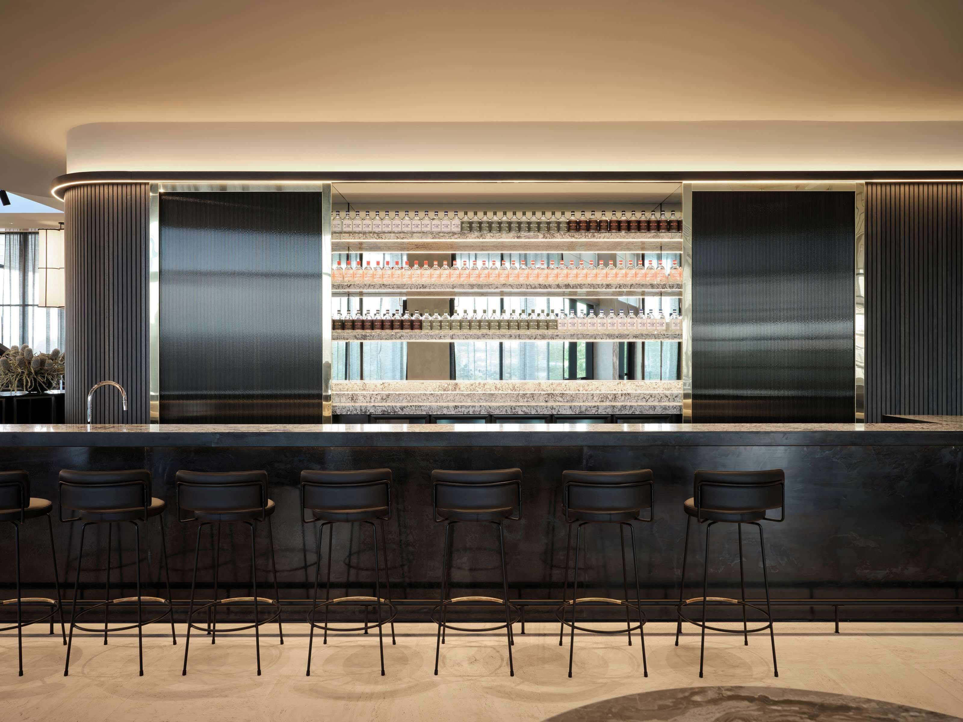 A modern bar area with a marble countertop, multiple shelves of bottled beverages, and six black bar stools.