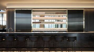 A modern bar area with a marble countertop, multiple shelves of bottled beverages, and six black bar stools.
