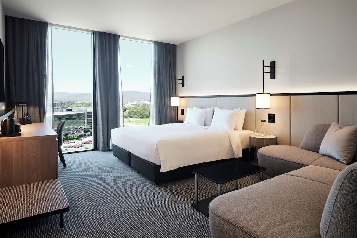 A hotel room with a large bed, a desk, a sofa, and a view of the cityscape.