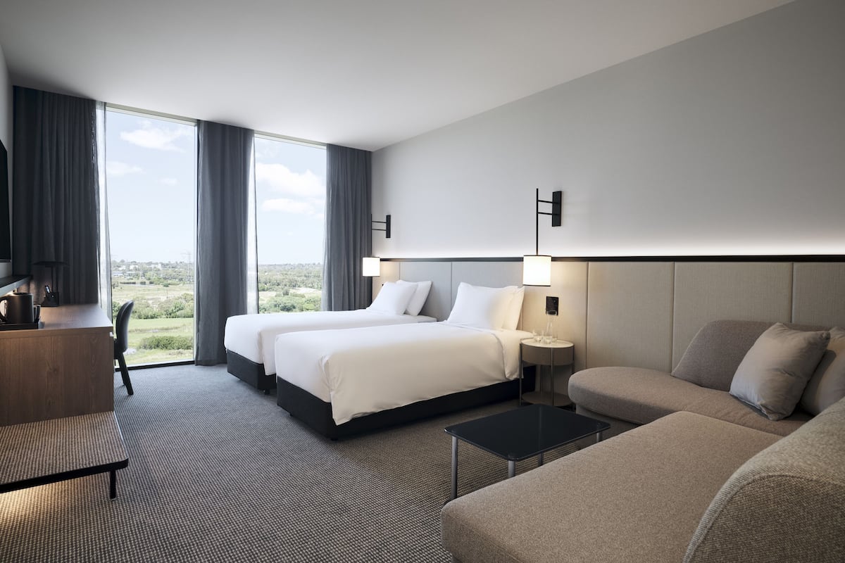 A hotel room with two beds, a sofa, a desk, and a view of the outdoors.