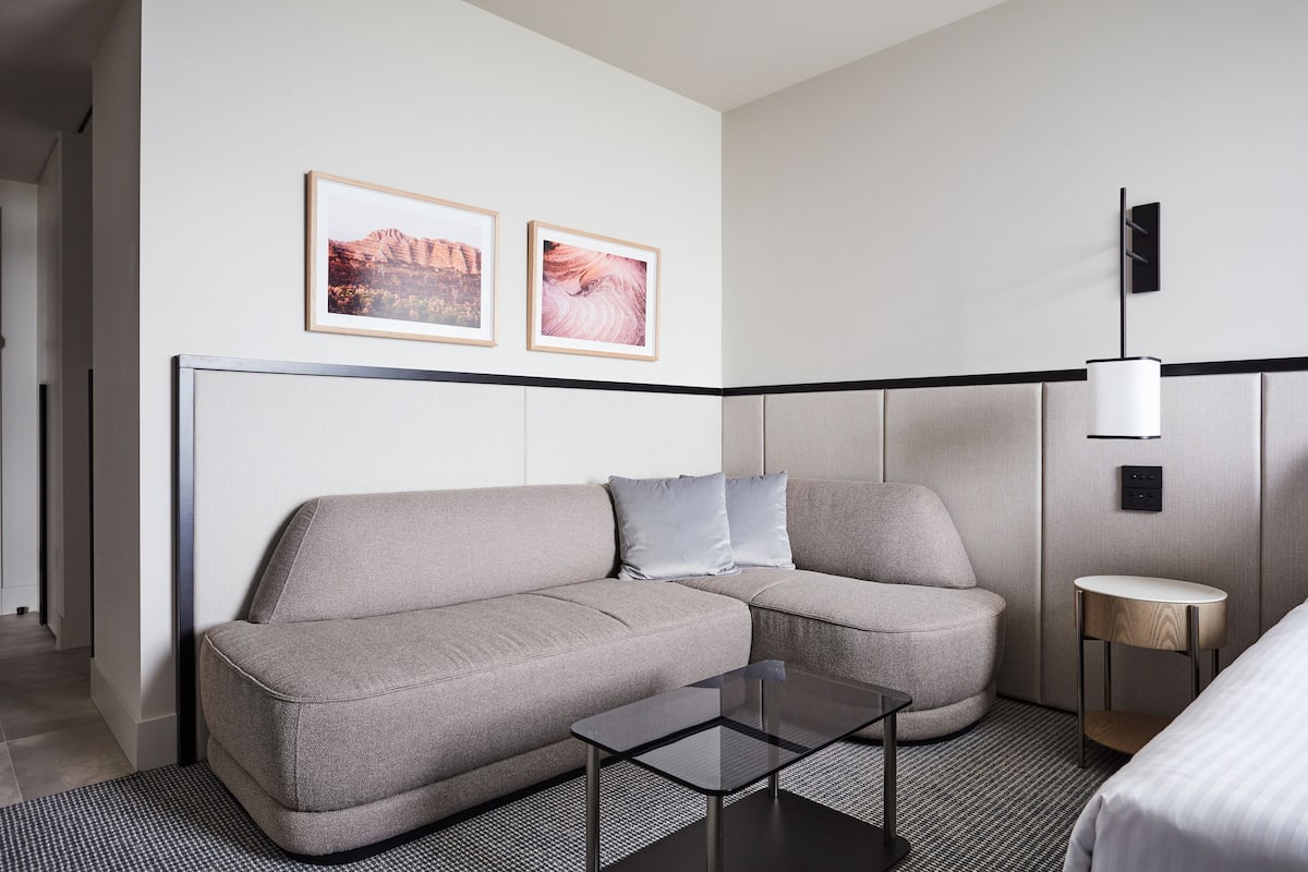 A modern hotel room with a grey sofa, a small round table, and two framed pictures on the wall.