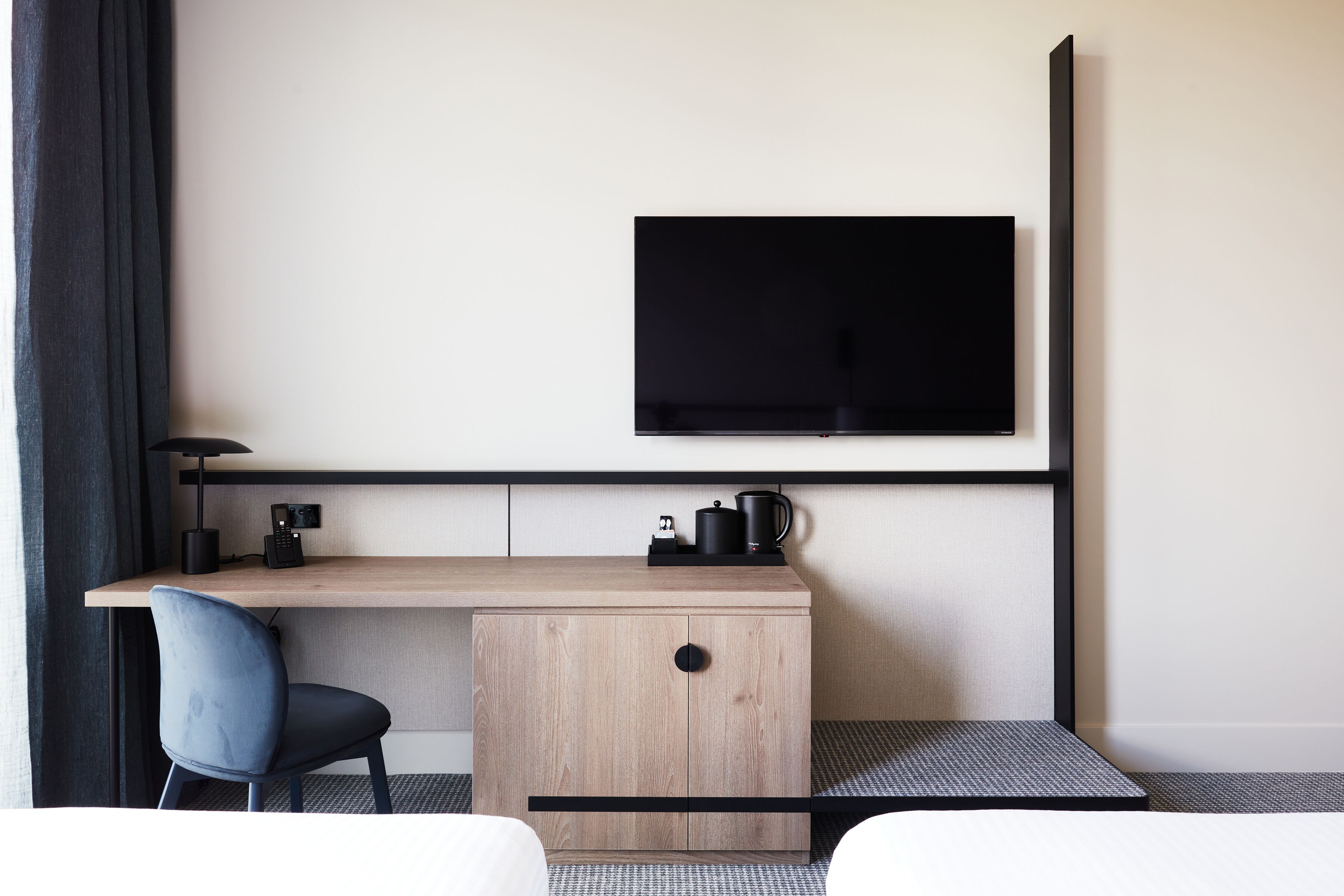 Ett modernt hotellrum med ett skrivbord i trä, en svart stol, en platt-TV som är monterad på väggen och en liten kaffestation.