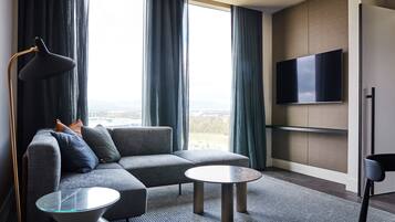 A modern living room with a sectional sofa, two round coffee tables, a floor lamp, and a flat-screen TV mounted on the wall.
