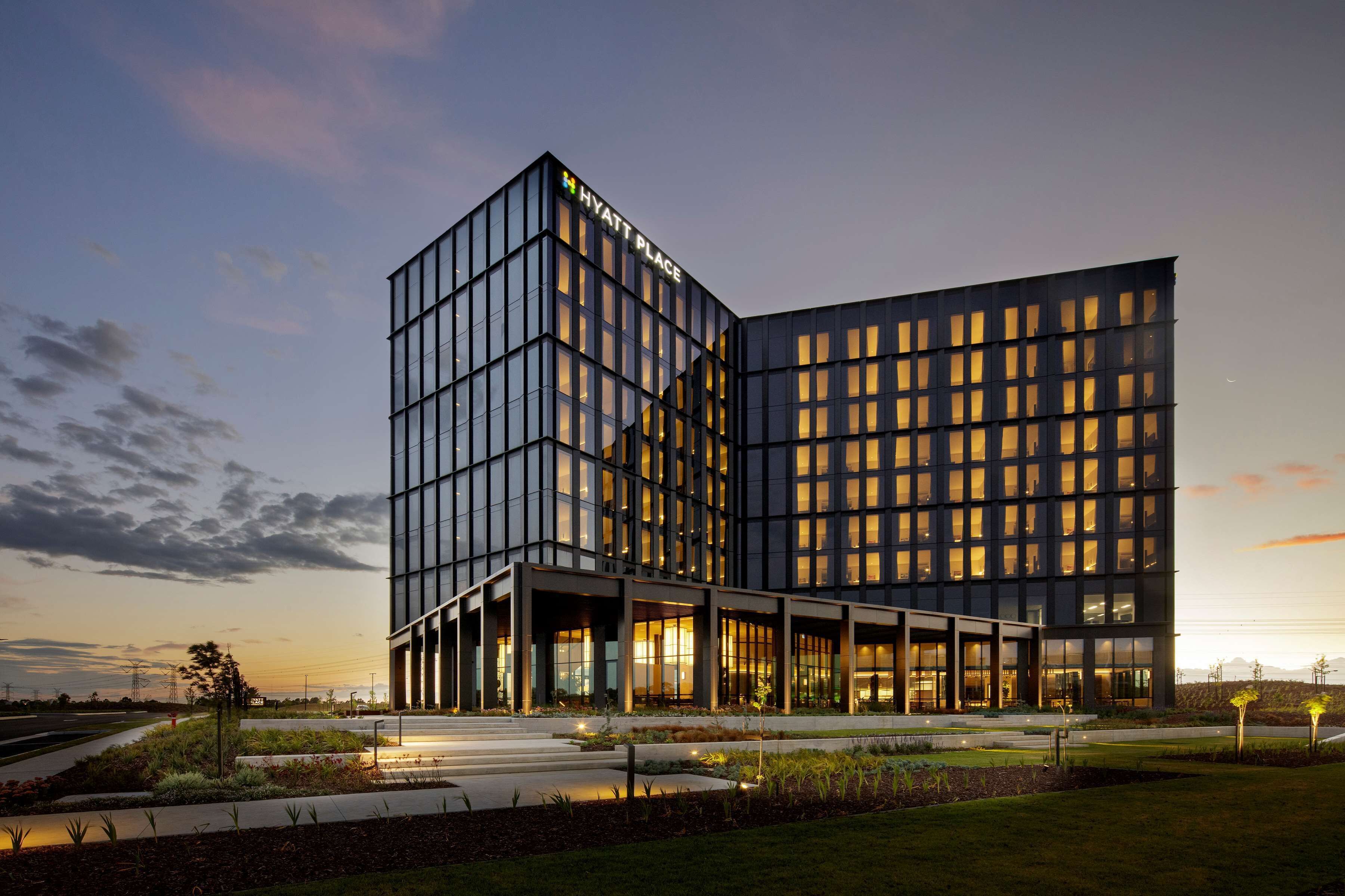 A modern hotel with a glass facade, a prominent 'Hyatt Place' sign, and a landscaped entrance area.