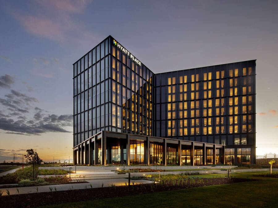 A modern hotel with a glass facade, a prominent 'Hyatt Place' sign, and a landscaped entrance area.