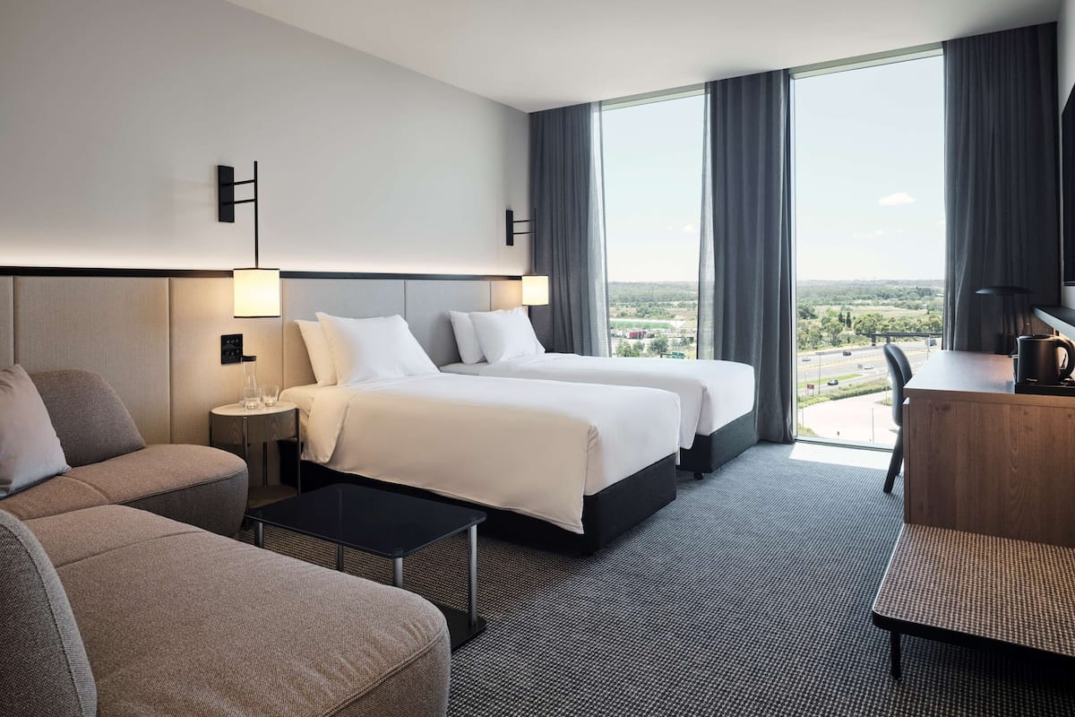 A hotel room with two beds, a sofa, a desk, and a view of the city.