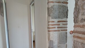A hallway with wooden flooring, a brick wall, and a white door. - O Nature, cherish my wishes before they run away (Francescas)