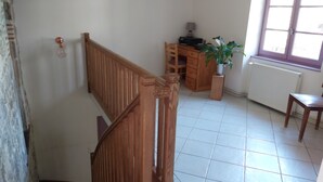 A staircase with wooden railings, a wooden desk with a computer, a potted plant, and a radiator in a room with tiled flooring. - O Nature, cherish my wishes before they run away (Francescas)