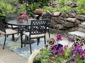 An outdoor patio with a round table and chairs, surrounded by a garden with rocks and flowers. - Gorgeous Garden Getaway, Near Cafes, Parks (Seattle)