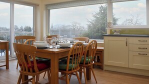 A dining area with a table set for four, wooden chairs, and a view of a cityscape through large windows. - Ideally positioned in a peaceful location enjoying extensive fell views. (Keswick)