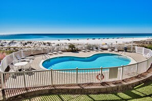 A swimming pool with a wooden deck and white chairs, surrounded by a white fence, overlooking a beach. - Windancer 201. Gulf Front, Free Beach Service, Pool, Grill, Beautiful Views! (Miramar Beach)