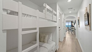 Camera con letto a castello, una scrivania, una sedia, vista sul balcone e corridoio che conduce a una sala da pranzo.