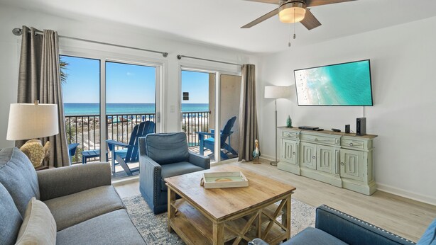 Un soggiorno con vista sulla spiaggia, un ventilatore a soffitto, una televisione a schermo piatto e un tavolino in legno.