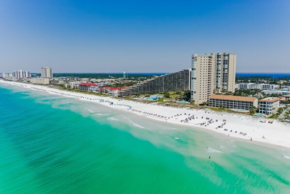 An aerial view of a coastal city with a beach, high-rise buildings, and a clear sky.