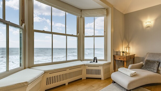 A room with a large bay window overlooking the sea, a cozy seating area with a cushioned bench, a small table with a lamp, and a rug on the floor. - 2 bedroom accommodation in Cromer (Cromer)