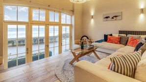 A spacious living room with a large window overlooking the sea, a comfortable sofa set, a glass coffee table, and a chandelier. - 2 bedroom accommodation in Cromer (Cromer)