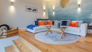 A modern living room with a white sofa, a glass coffee table, and a wooden staircase. - 2 bedroom accommodation in Cromer (Cromer)