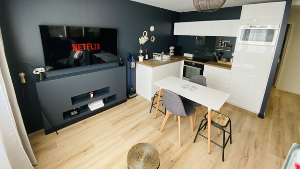 Une cuisine moderne avec un coin repas, un téléviseur diffusant du contenu « NETFLIX », et un luminaire suspendu original.