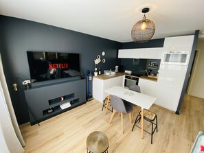 A modern kitchen with a dining area, a TV displaying 'NETFLIX', and a unique hanging light fixture.