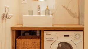 Une petite salle de bain avec un miroir rond, un lavabo, un lave-linge et un panier en osier.