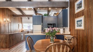A modern kitchen with dark cabinets, a central island, and a dining area with wooden chairs and a vase of flowers. - Walk to Village - Bike Path Access - Pet Friendly 2 BR - Gear Storage - Sleeps 6 (Mammoth Lakes)