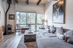 Un salon moderne avec une cheminée, un canapé, une table basse et une grande fenêtre donnant sur la forêt.