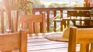 A wooden deck with a table and chairs, a woven mat, and a plant in a glass vase. - Apartment-Royal-Wet room-Partial sea view-Piscine et Salle de Sport (La Trinité)