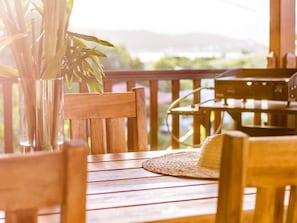 A wooden deck with a table and chairs, a woven mat, and a plant in a glass vase. - Apartment-Royal-Wet room-Partial sea view-Piscine et Salle de Sport (La Trinité)