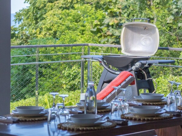 A dining area with a table set for a meal, a grill, and a view of greenery.
