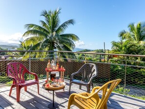 Eine Terrasse mit Stühlen und einem Tisch, mit Blick auf eine üppige Landschaft mit Palmen und blauem Himmel.