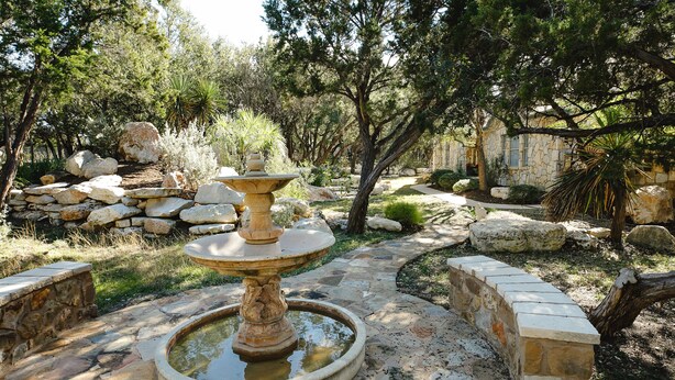 Una fuente de piedra rodeada de rocas y árboles en un jardín.